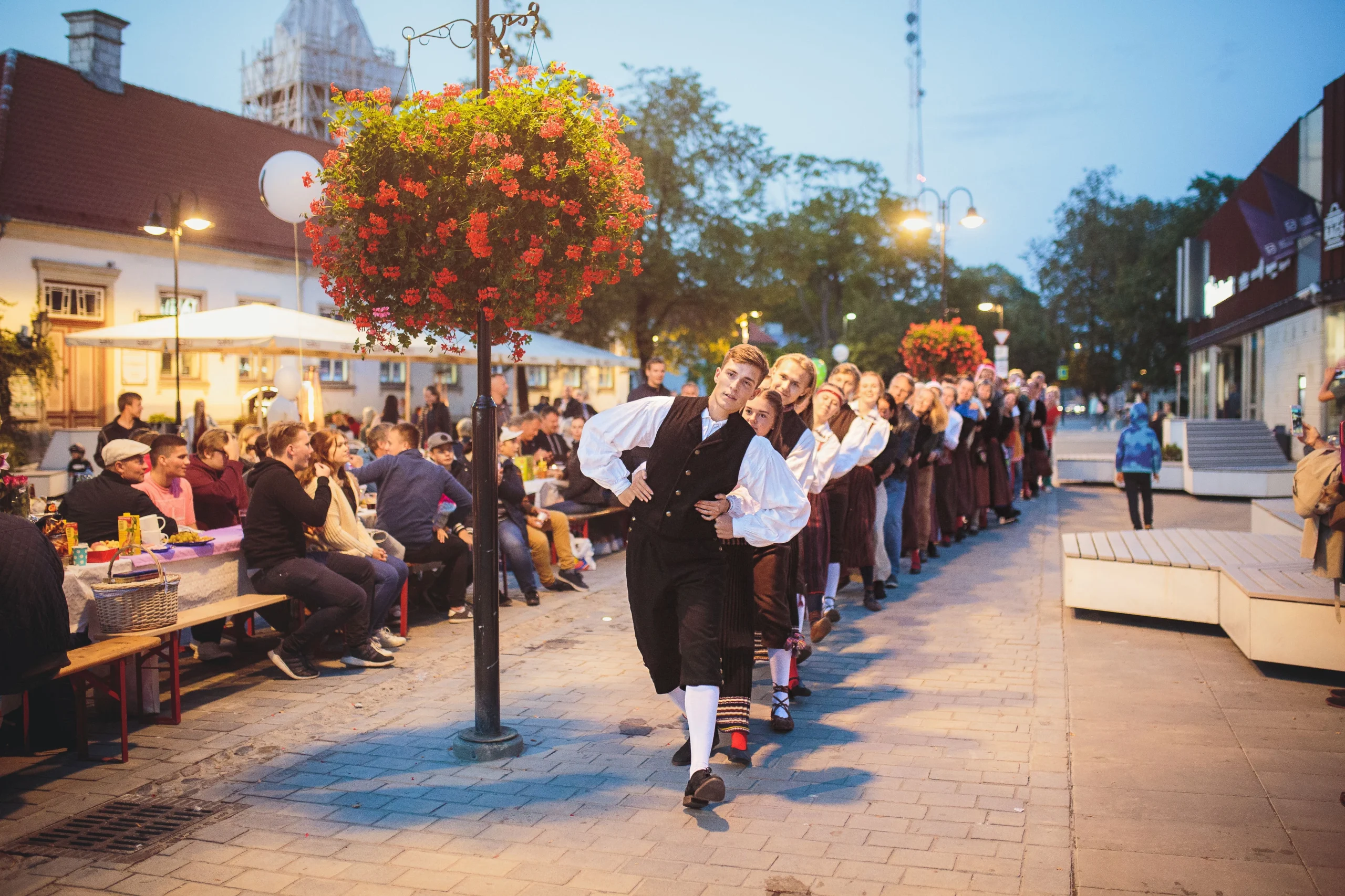 Valmar Voolaiu foto rahvatantsijatest esinemas pika rahvast täis söögilaua kõrval tänavapiknikul Kuressaare kesklinnas.